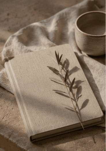 Taccuino di lino con ramo d'ulivo e ciotola in ceramica, luce calda